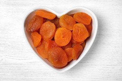 Photo of Bowl of dried apricots on white wooden table, top view. Healthy fruit