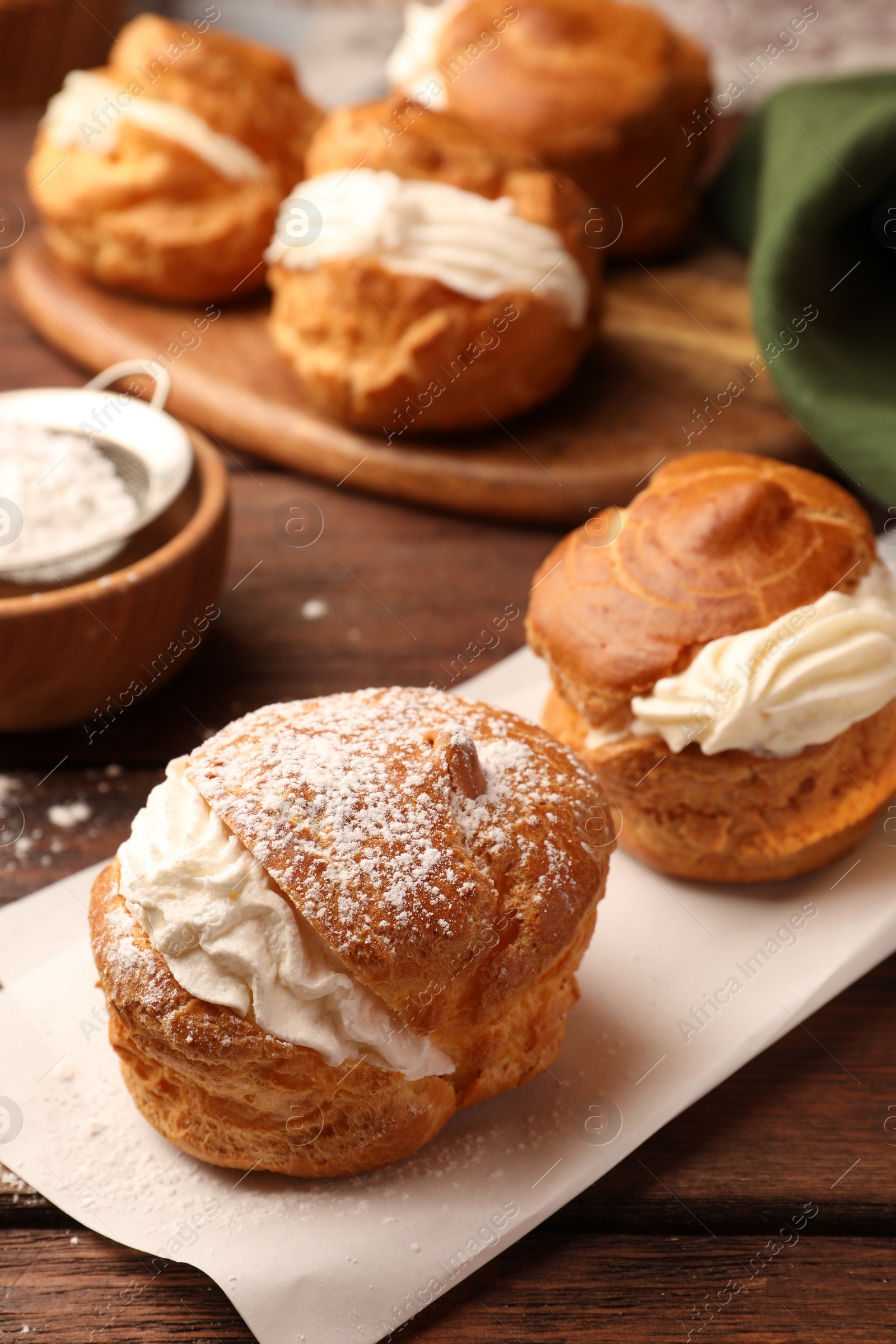 Photo of Delicious profiteroles with cream filling and powdered sugar on wooden table, closeup