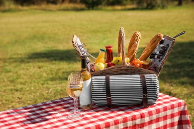 Picnic basket with wine, snacks and mat on table in park. Space for text