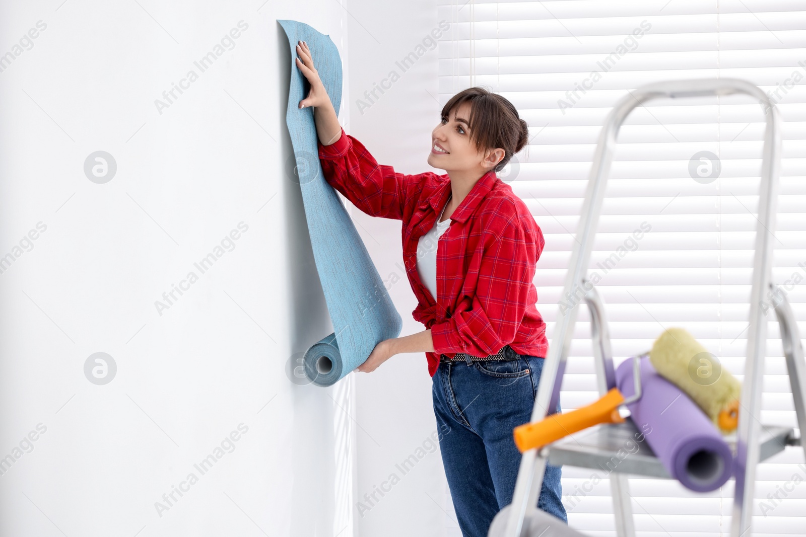 Photo of Woman hanging light blue wallpaper in room