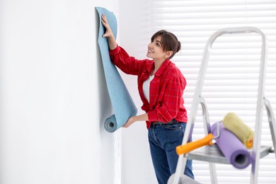 Woman hanging light blue wallpaper in room