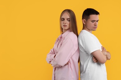 Portrait of resentful couple with crossed arms on orange background, space for text