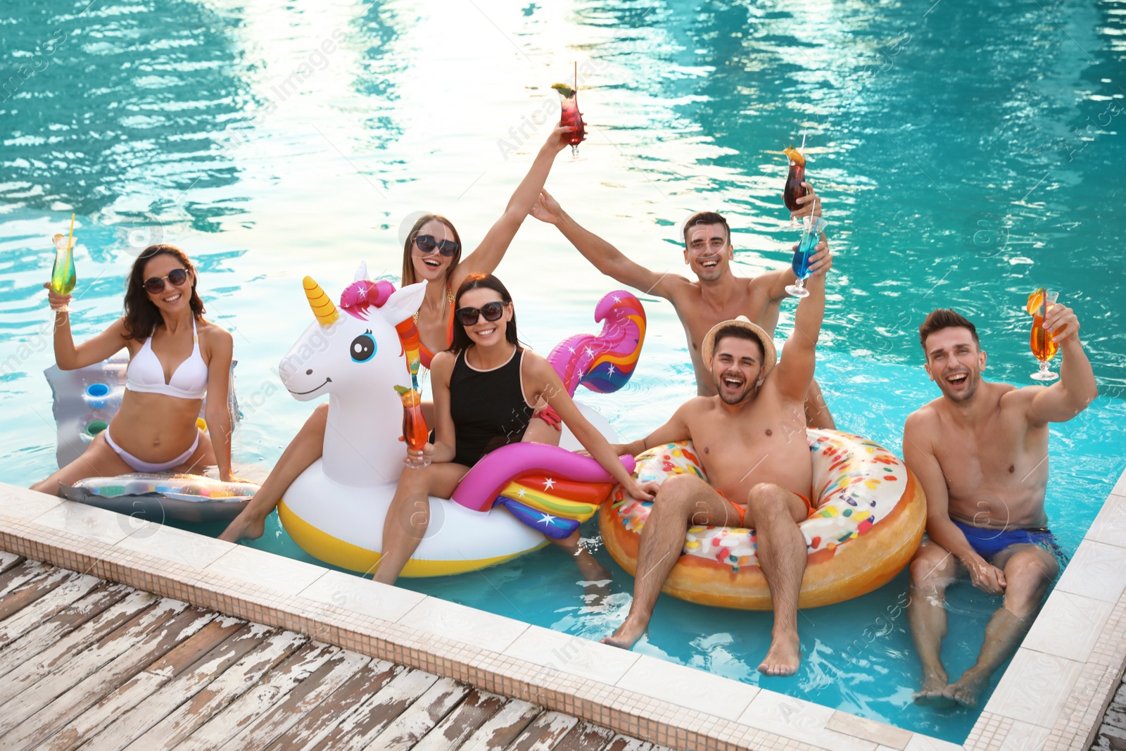 Photo of Happy young friends with refreshing cocktails relaxing in swimming pool