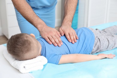 Orthopedist massaging child's back in clinic, closeup. Scoliosis treatment