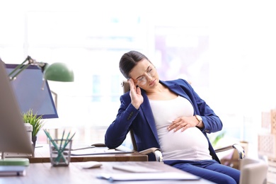 Photo of Young pregnant woman suffering from pain while working in office