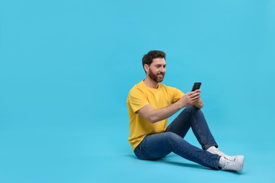 Photo of Smiling man with smartphone on light blue background. Space for text