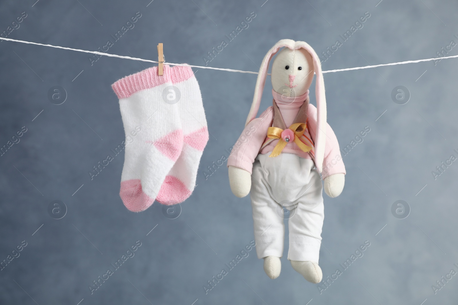Photo of Pair of child's socks and toy bunny hanging on laundry line against dark background