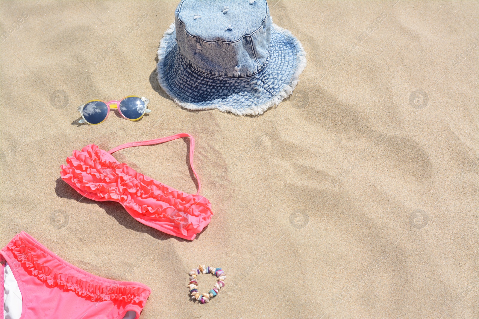 Photo of Jeans hat, sunglasses and bikini on sand, space for text. Beach accessories