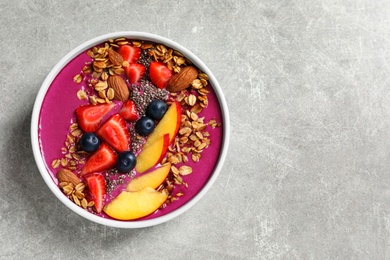 Photo of Delicious acai smoothie with granola and berries in bowl on grey table, top view. Space for text