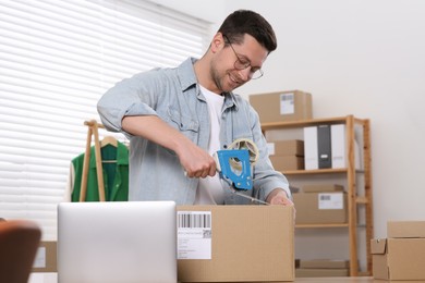 Photo of Seller taping parcel at workplace in office. Online store