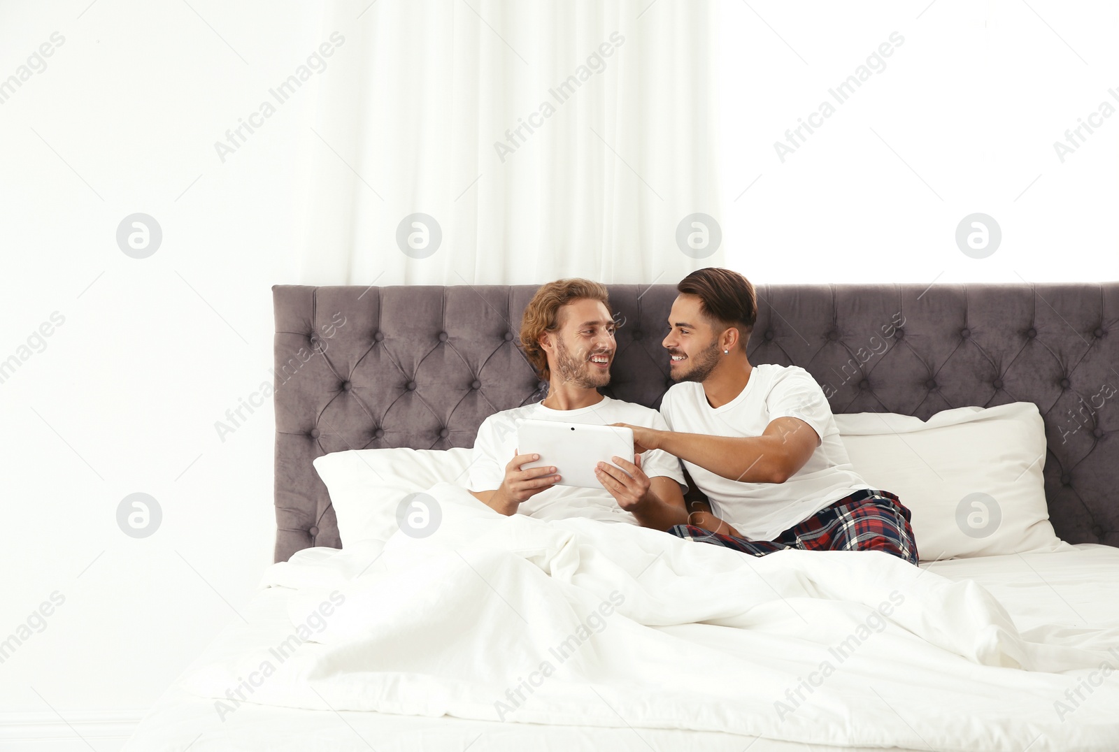 Photo of Happy gay couple with tablet computer on bed at home