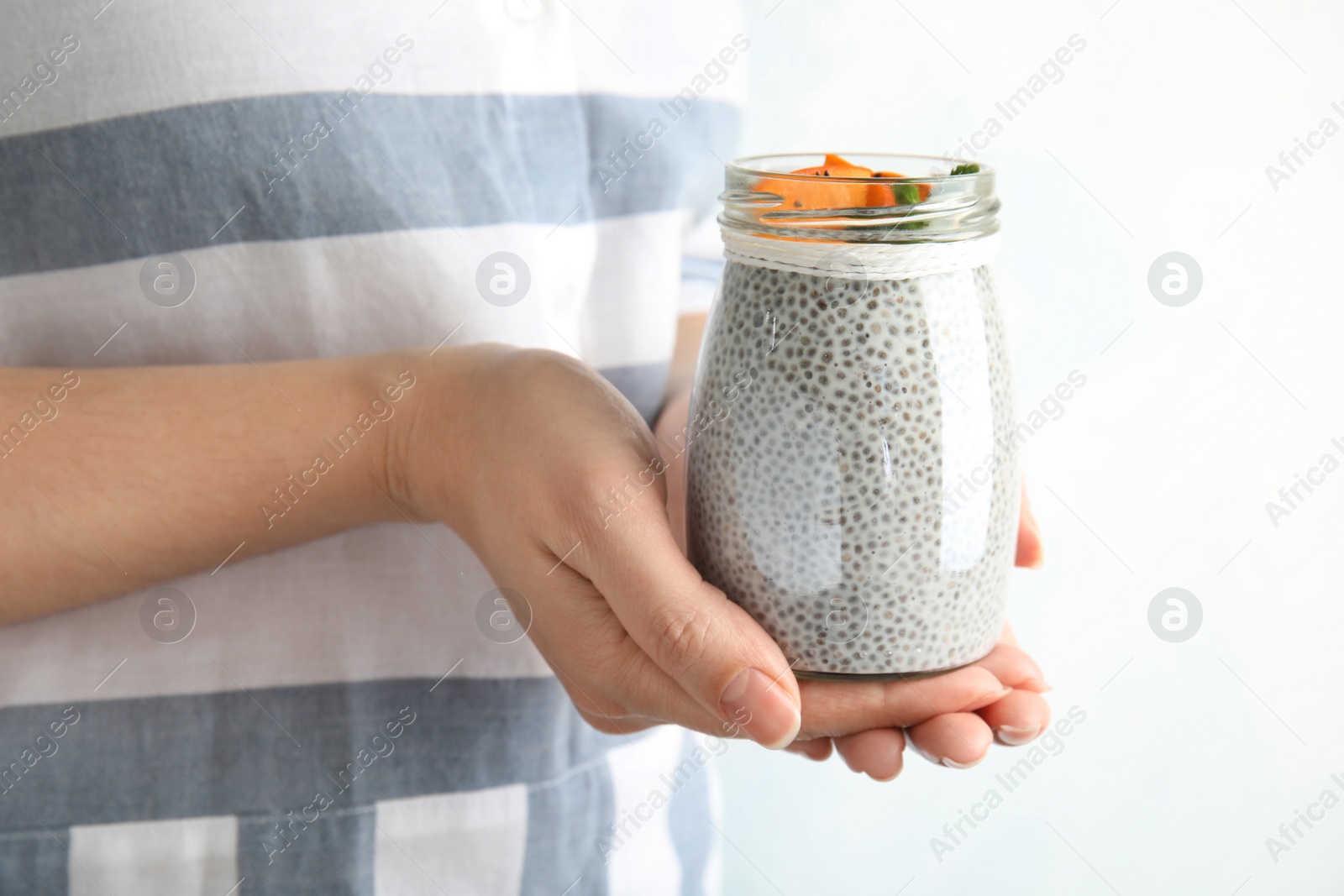 Photo of Young woman holding jar of tasty chia seed pudding with persimmon, closeup