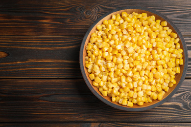 Photo of Delicious canned corn in bowl on wooden table, top view. Space for text