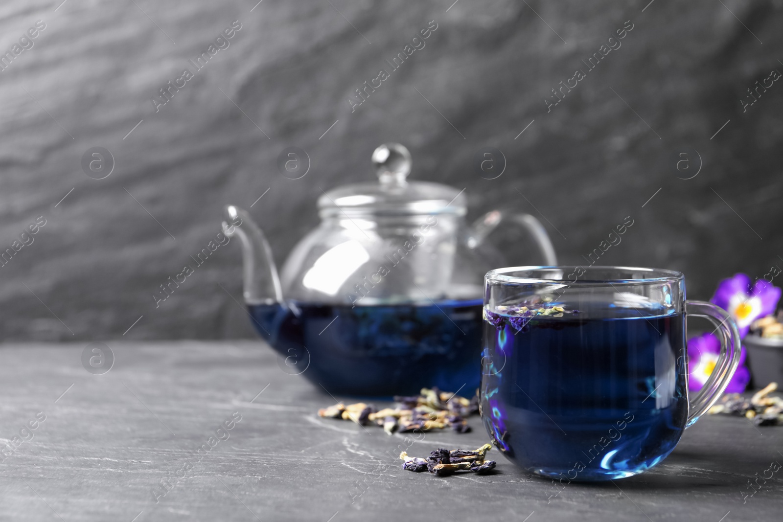 Photo of Glass cup of organic blue Anchan on black table, space for text. Herbal tea