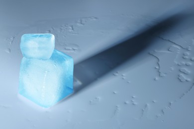 Photo of Crystal clear ice cubes on light blue background, space for text