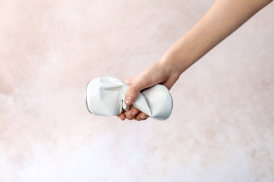 Woman holding crumpled aluminum can on light background. Metal waste recycling