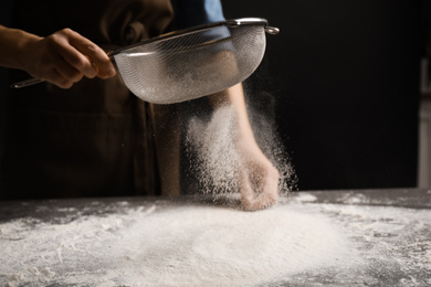 Photo of Woman sifting flour at grey table, closeup. Making pasta