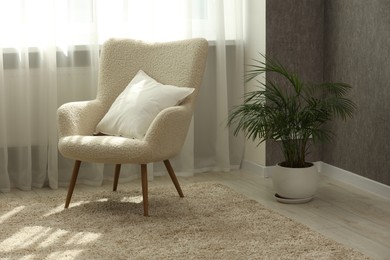 Photo of Soft white pillow on armchair and houseplant near window indoors