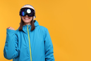 Winter sports. Happy woman with snowboard goggles on orange background, space for text
