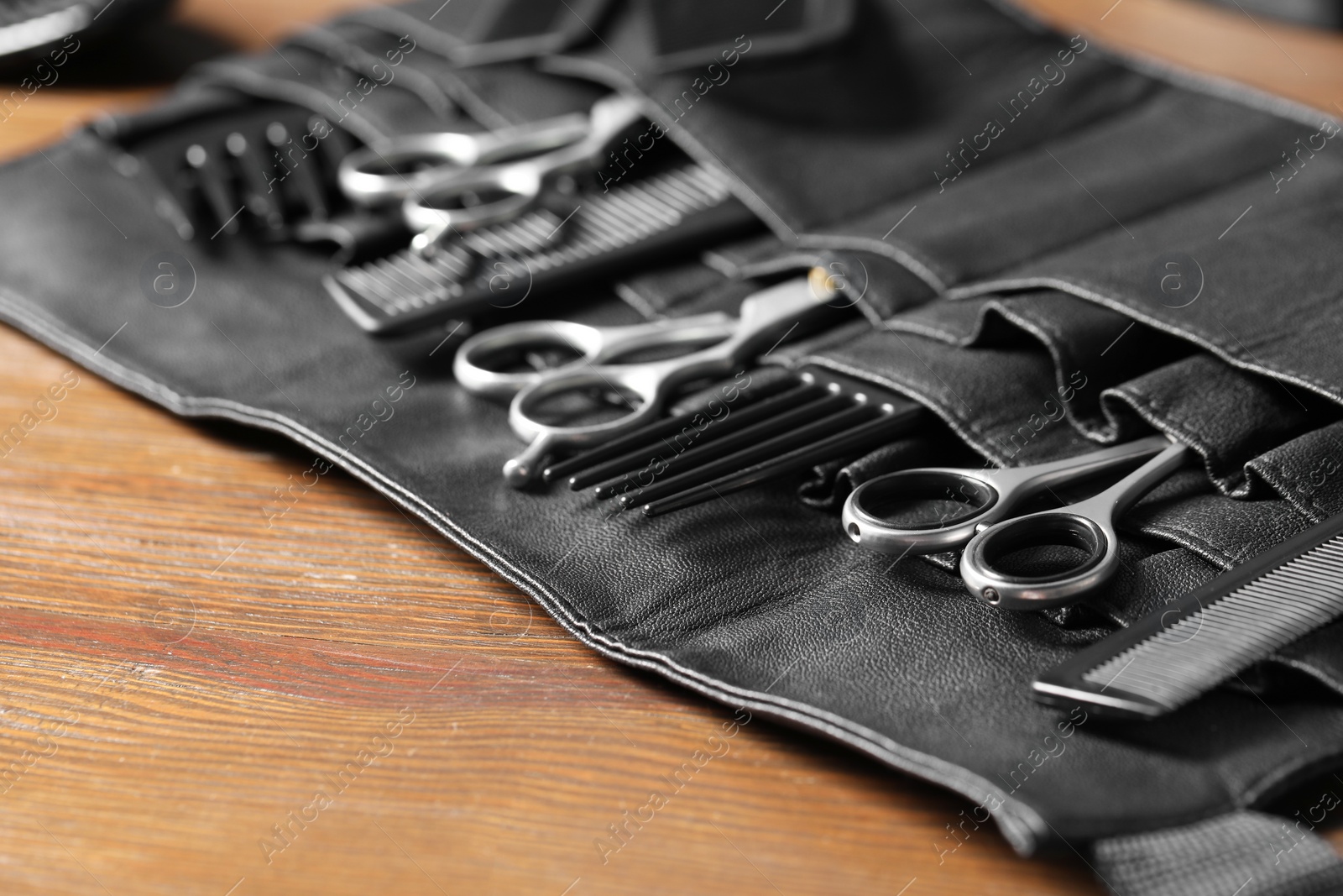 Photo of Hairdresser tools. Professional scissors and combs in leather organizer on wooden table, closeup