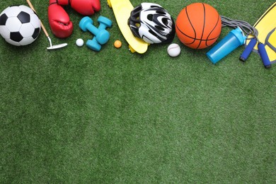 Different sport equipment on green grass, flat lay. Space for text