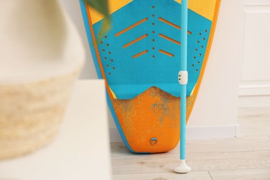 Photo of SUP board and paddle on wooden floor in room