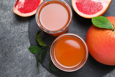 Tasty freshly made grapefruit juice and fruits on grey table, flat lay 