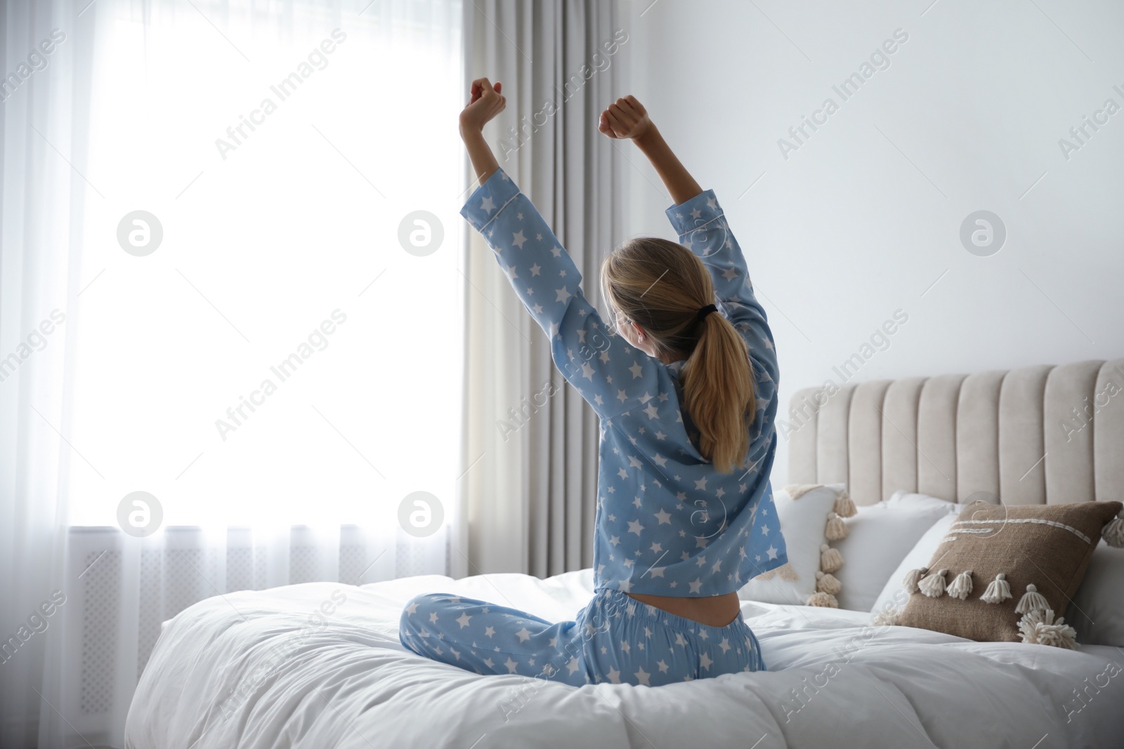 Photo of Young woman stretching on bed at home, back view. Morning fitness