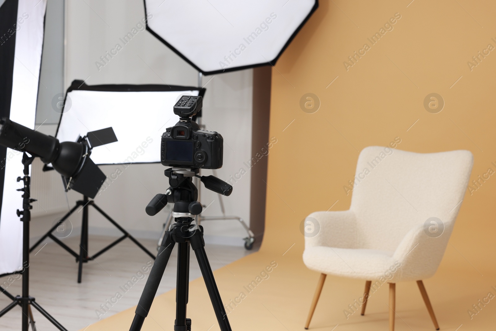 Photo of Camera on tripod, armchair and professional lighting equipment in modern photo studio, space for text