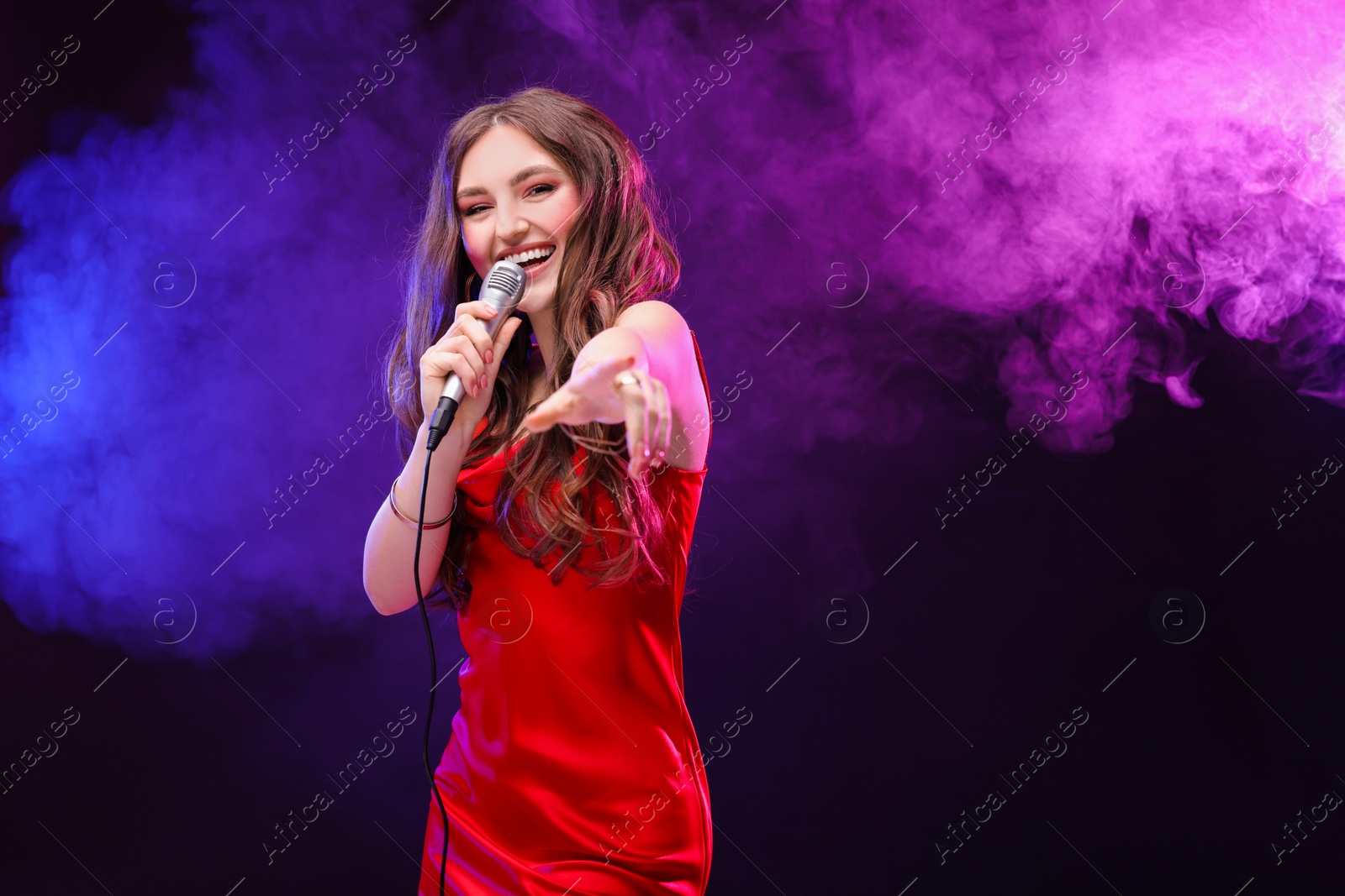 Photo of Emotional woman with microphone singing in color lights. Space for text