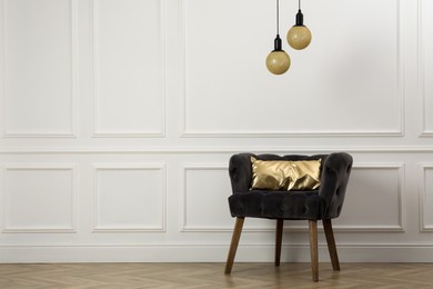 Photo of Stylish armchair with cushion near white wall indoors, space for text. Interior design