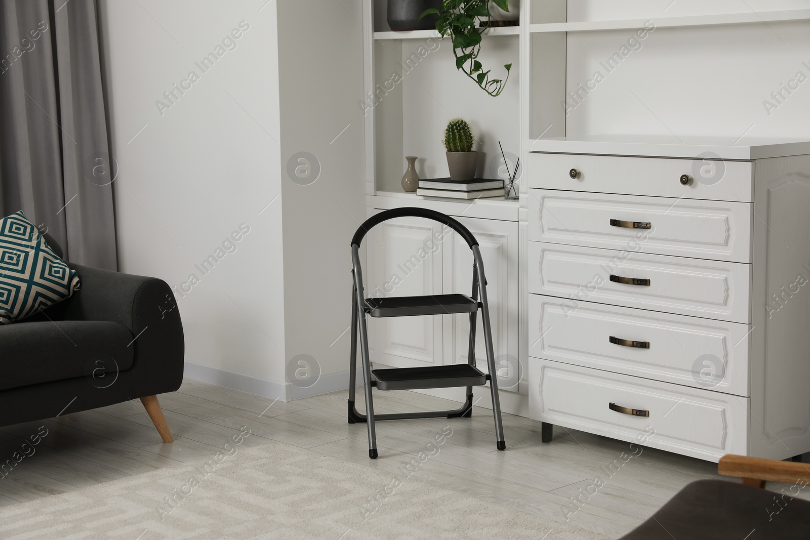 Photo of Metal folding ladder near chest of drawers and shelf with accessories in room