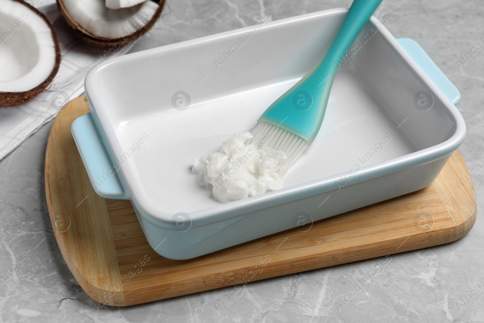 Photo of Baking dish with coconut oil and silicone brush on light grey table