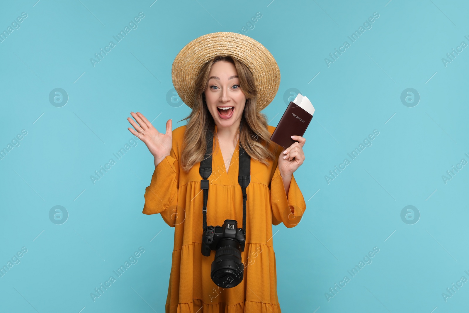 Photo of Emotional young woman with camera, passport, ticket and hat on light blue background