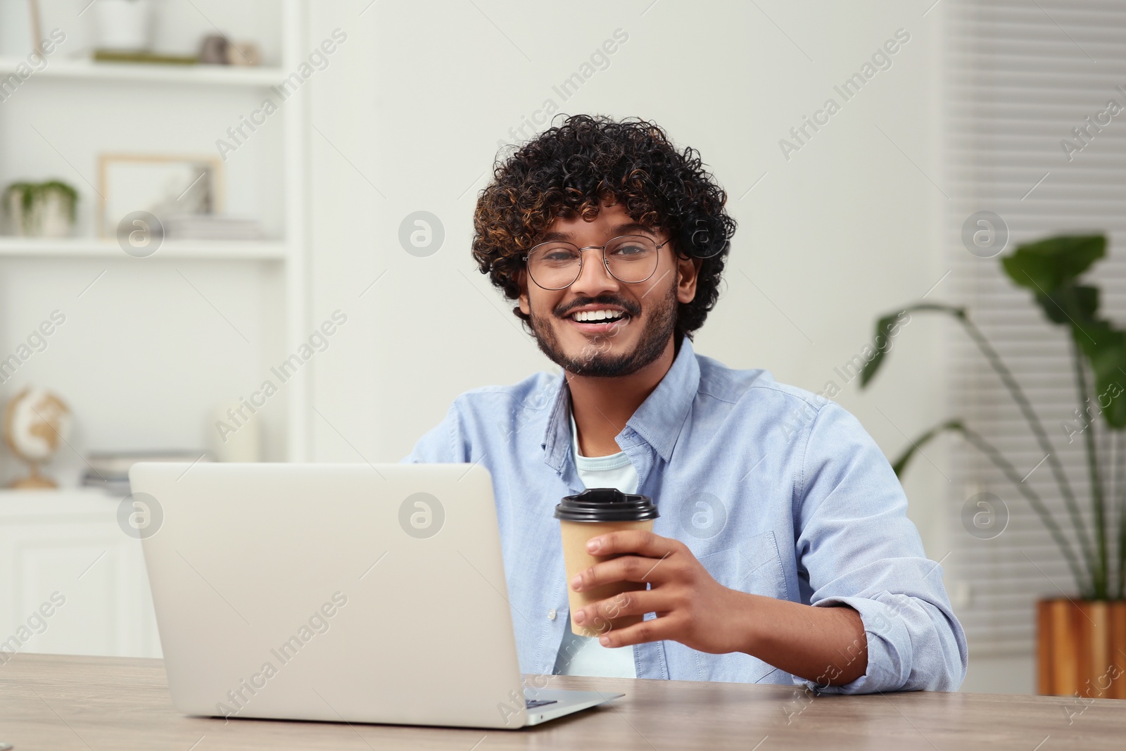 Photo of Handsome smiling man with coffee using laptop in room