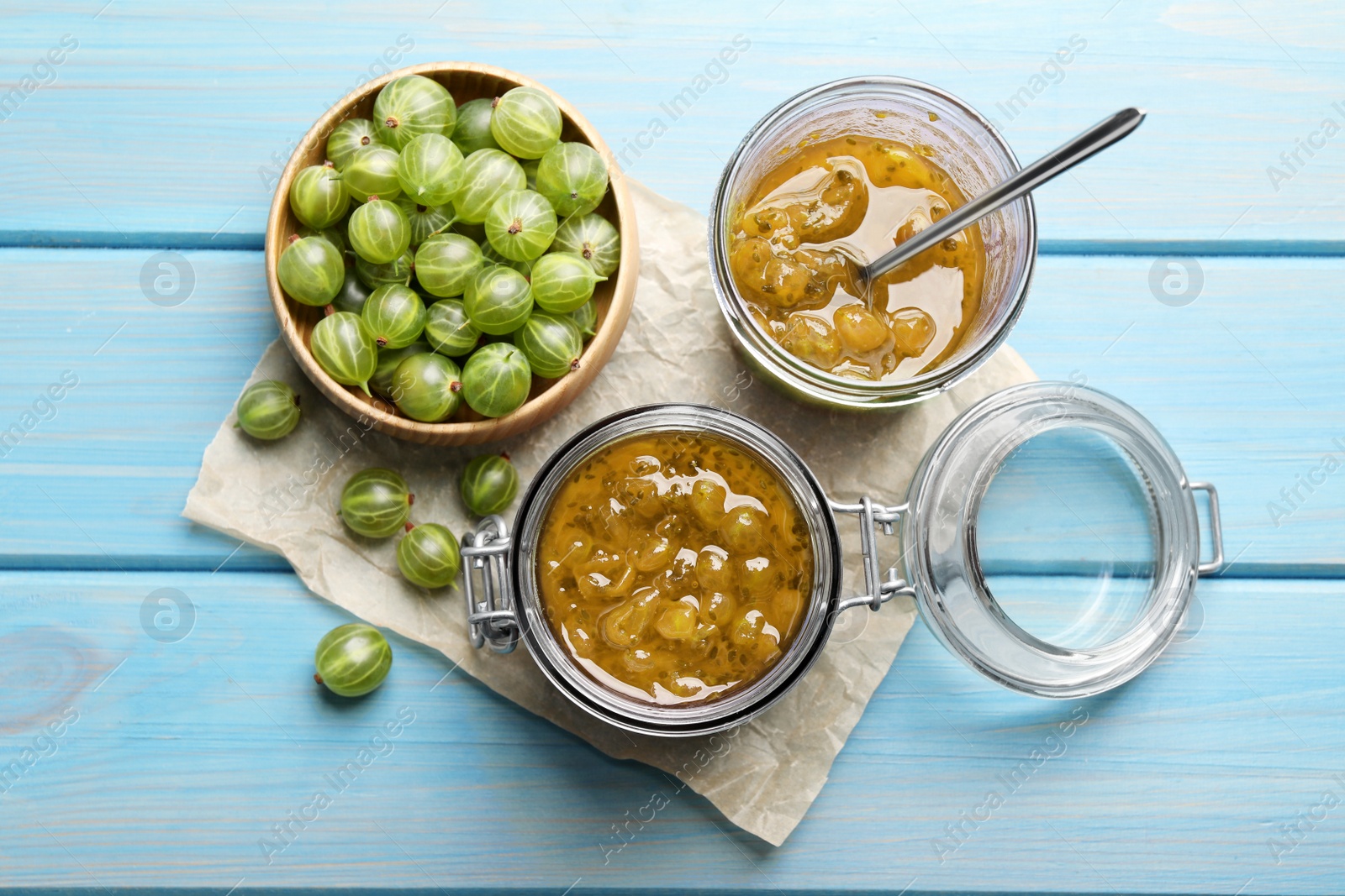 Photo of Flat lay composition with jars of delicious gooseberry jam and fresh berries on blue wooden table