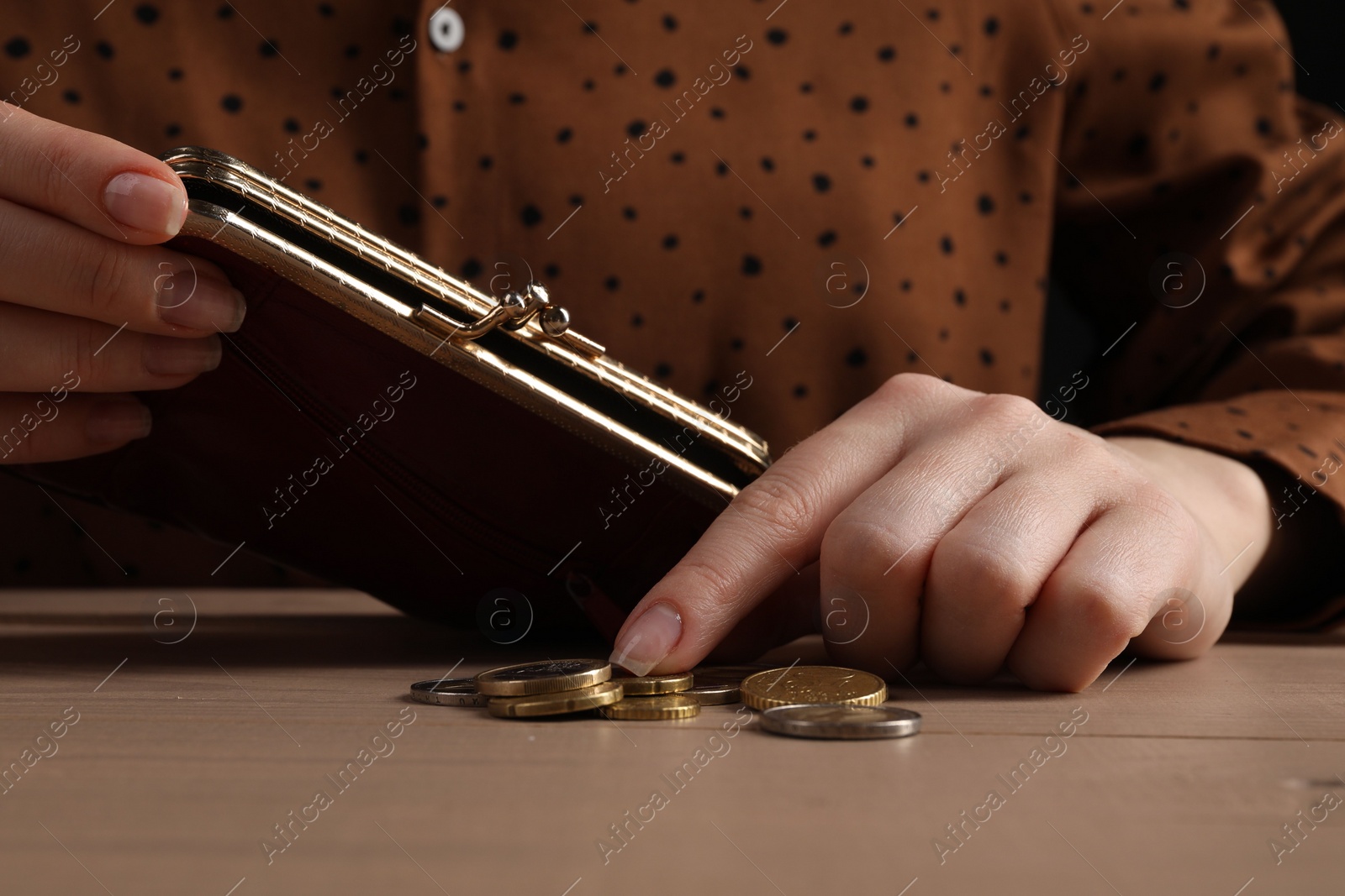 Photo of Poverty. Woman with wallet counting coins at wooden table, closeup