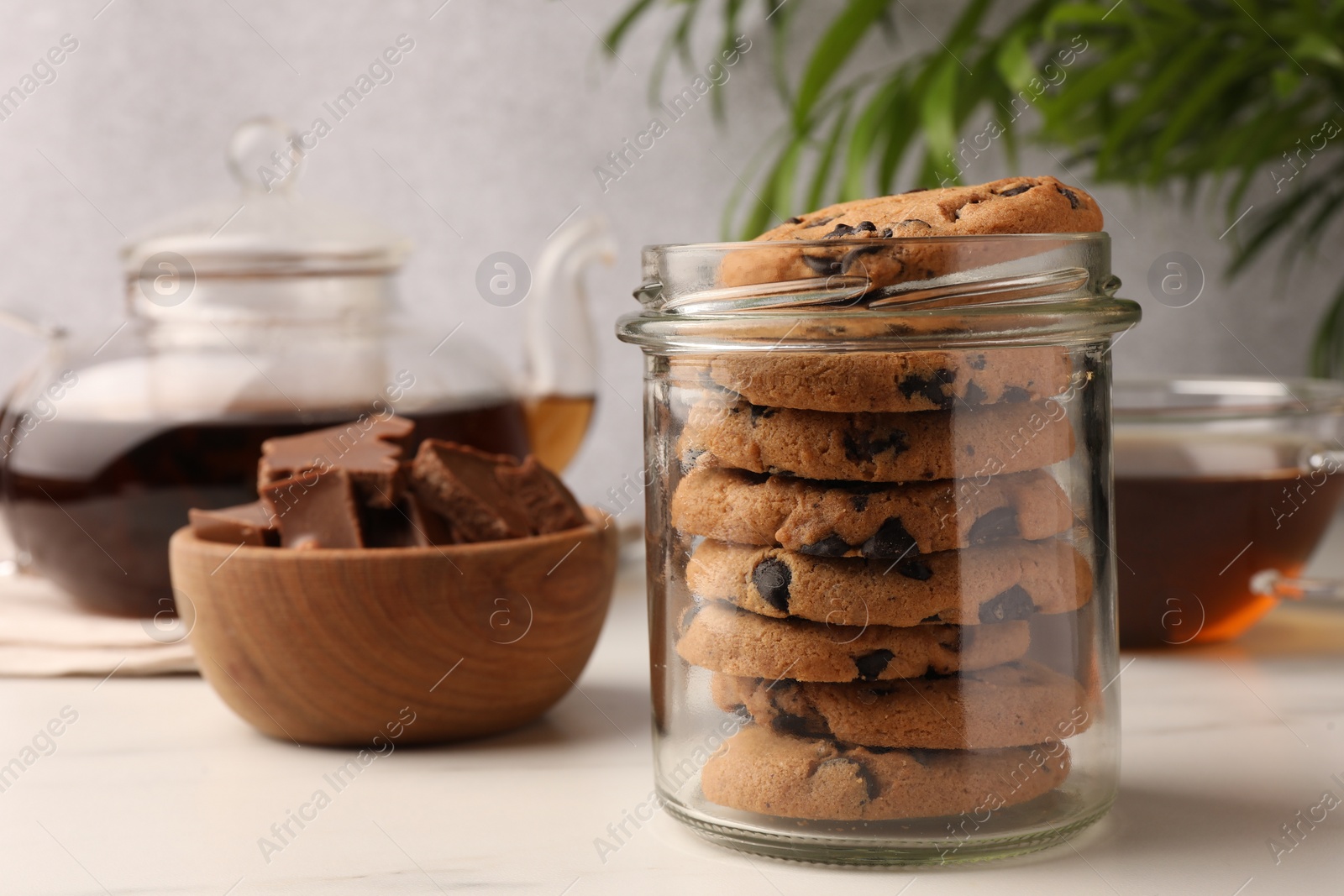 Photo of Glass jar with delicious chocolate chip cookies and tea on white marble table