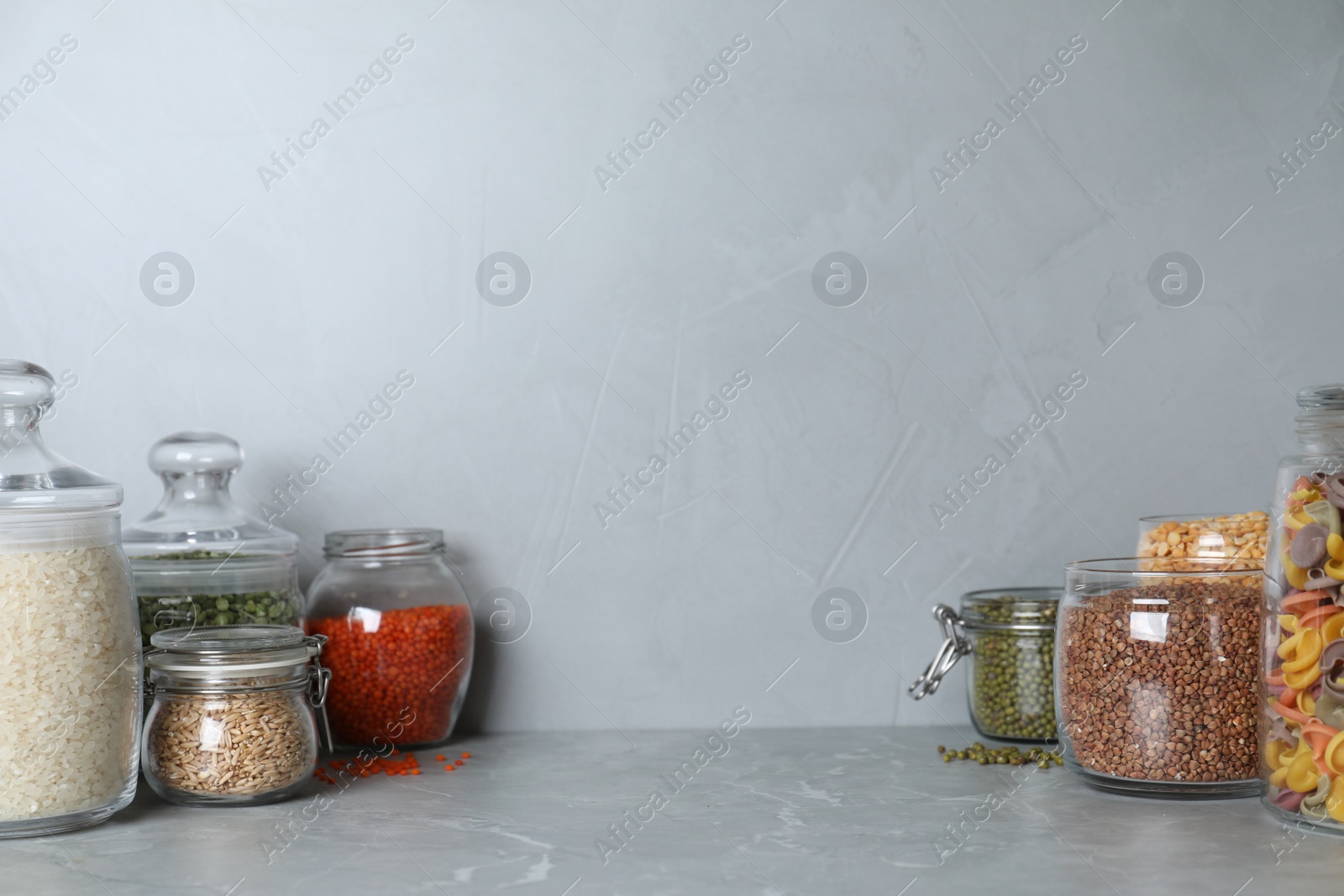 Photo of Glass jars with different types of groats on grey marble table