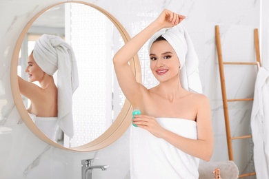 Photo of Beautiful young woman applying deodorant after shower in bathroom