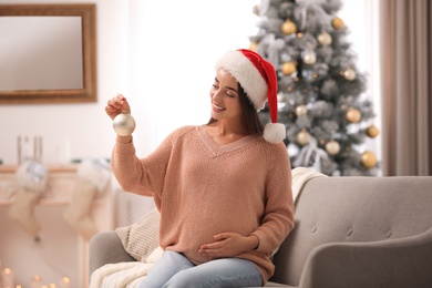 Happy pregnant woman with Christmas ball in living room. Expecting baby