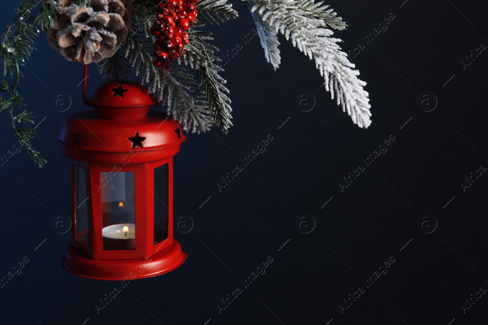 Photo of Christmas lantern with burning candle on fir tree against dark background, closeup. Space for text