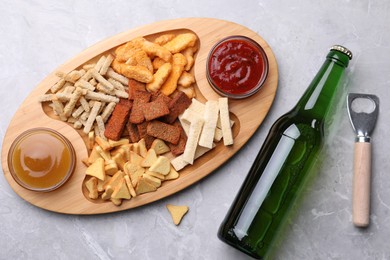Different crispy rusks served with dip sauces and beer on light marble table, flat lay