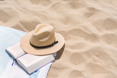 Photo of Beach towel with straw hat and book on sand. Space for text