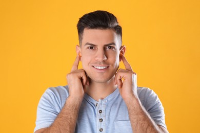 Photo of Man inserting foam ear plugs on yellow background