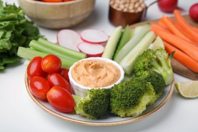 Photo of Plate with delicious hummus and fresh vegetables on white table, closeup