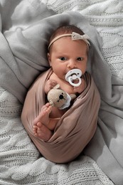 Photo of Adorable newborn baby with pacifier and toy on knitted plaid, top view