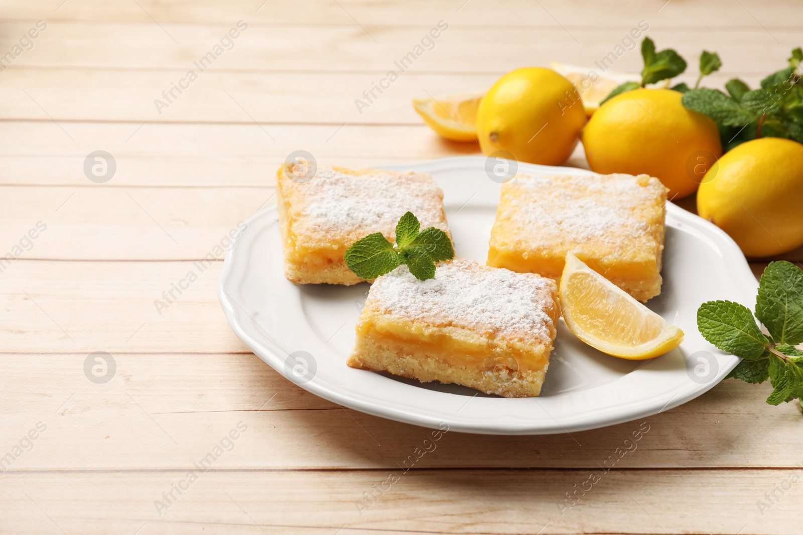 Photo of Tasty lemon bars with powdered sugar and mint on wooden table. Space for text