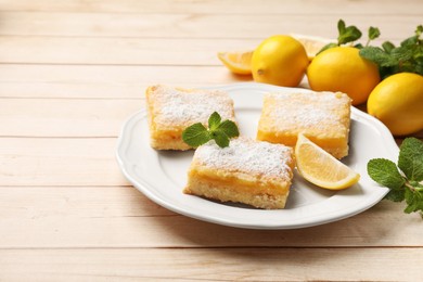 Tasty lemon bars with powdered sugar and mint on wooden table. Space for text
