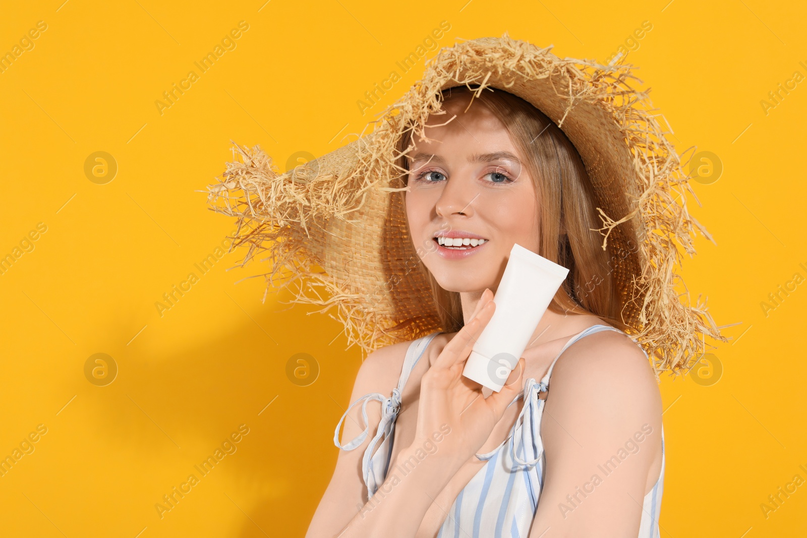 Photo of Beautiful young woman in straw hat holding sun protection cream on orange background, space for text